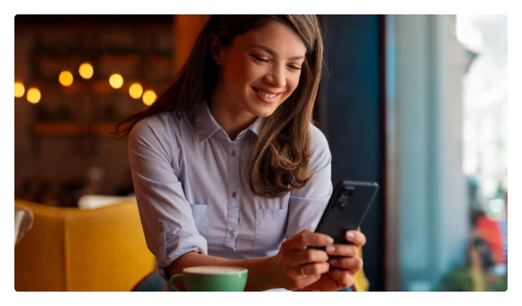 Smiling woman reading her phone over a cup of coffee