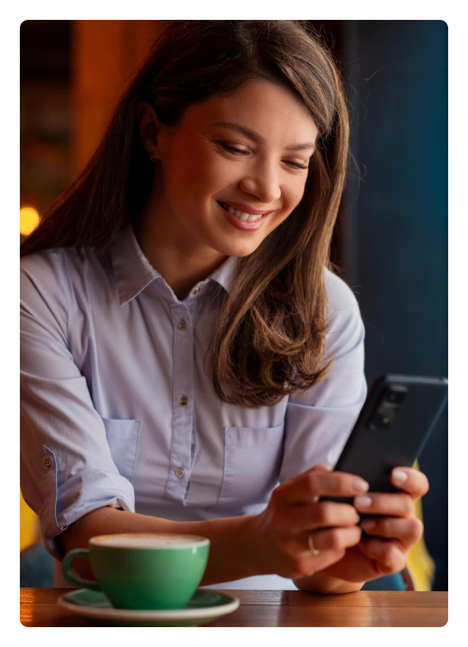 Smiling woman reading her phone over a cup of coffee