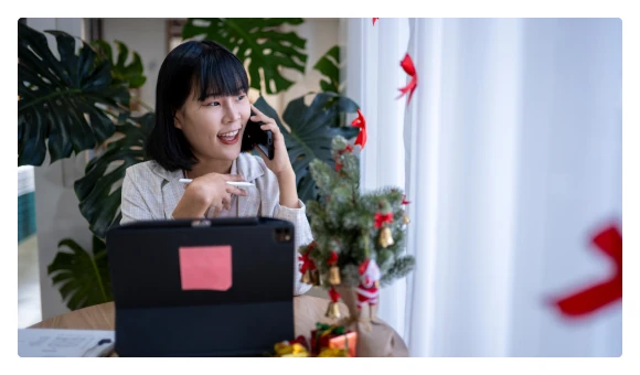 Woman on the phone beside her laptop and a Christmas tree