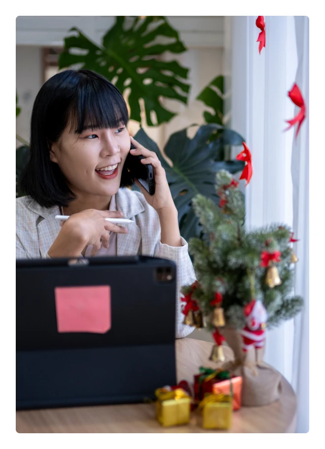 Woman on the phone beside her laptop and a Christmas tree