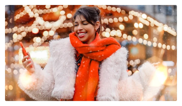 Smiling woman in a winter coat and an orange scarf among holiday lights
