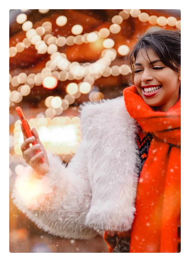 Smiling woman in a winter coat and an orange scarf among holiday lights
